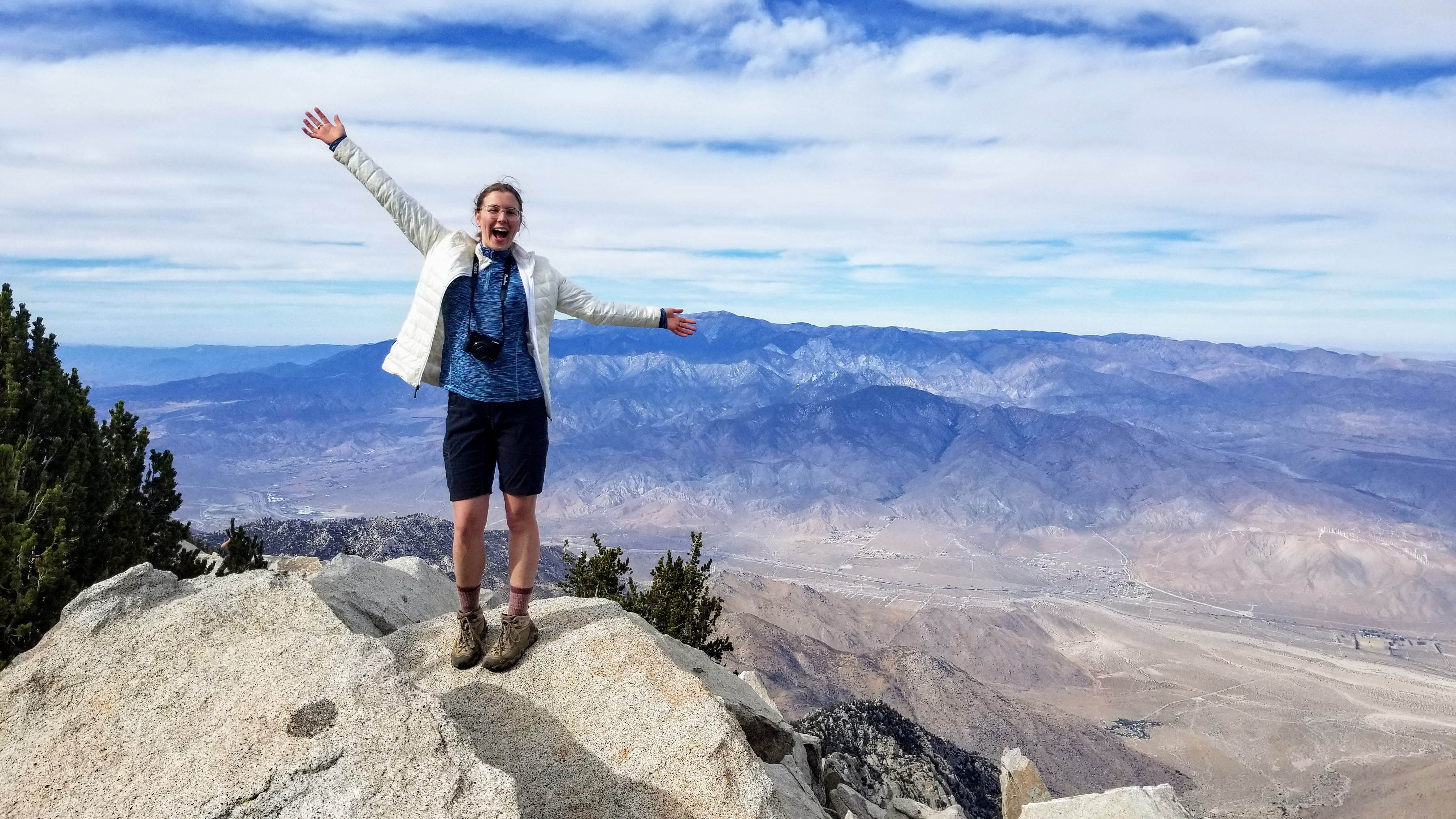 woman standing at vista point overlooking a dry valley, with snow-capped mountains in the distance