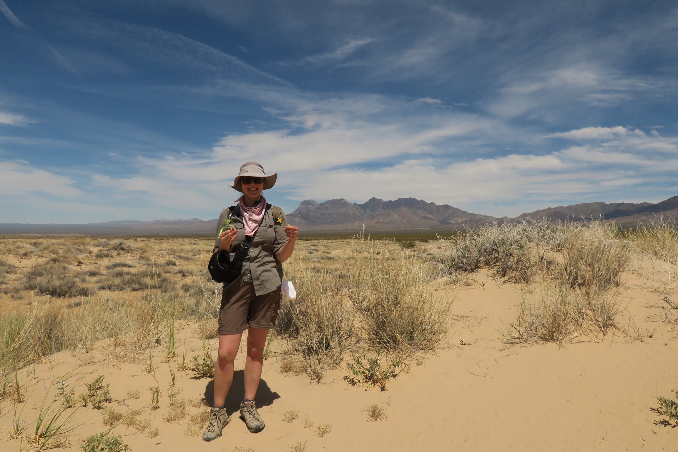 woman standing in the desert, smiling, wearing a wide-brimmed hat